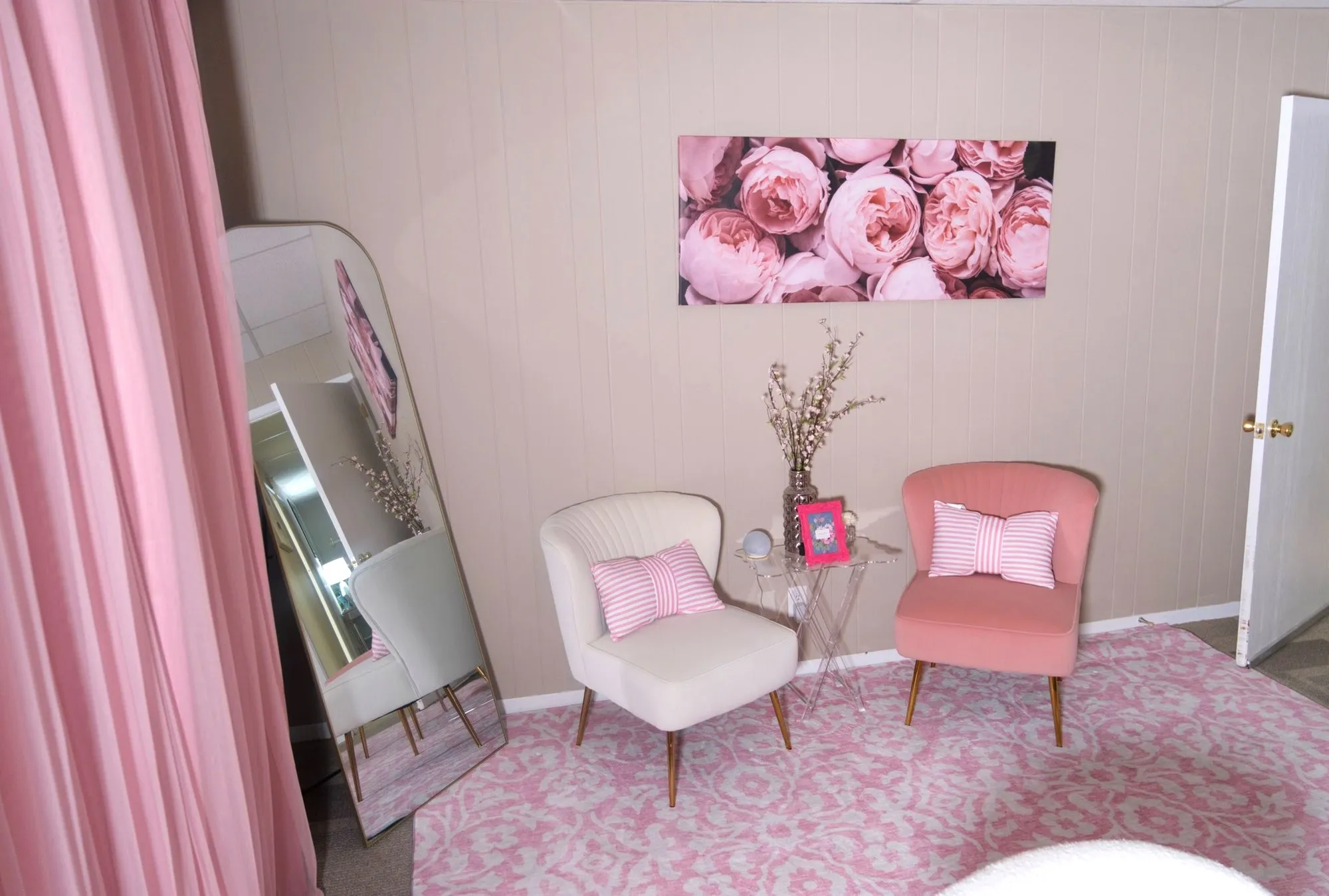 A seating nook at Felina Sno Wellness: a cream and a pink velvet chair under a peony print, beside a tall gold-framed mirror